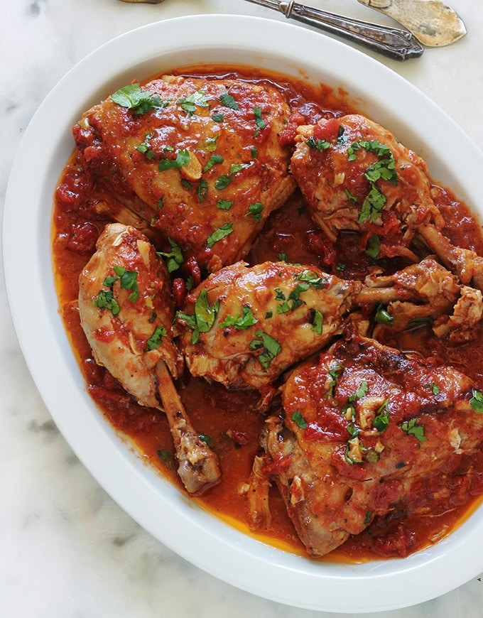 Cette recette de poulet à l’ail et tomates me vient de ma mère. C’est un plat savoureux et économique. Ce sont des morceaux de poulet cuits lentement et longuement dans une cocotte ou une grande poêle avec de l’ail et des tomates. Pas besoin de laisser mariner le poulet au préalable. Après cuisson, le poulet est très tendre, juteux et plein de saveurs.