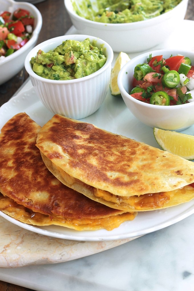 Apprenez comment faire les quesadillas mexicaines. C’est facile, rapide et vous pouvez les garnir de mille et une façons, avec ou sans viande. Ce sont des tortillas mexicaines, garnies de fromage, et éventuellement des légumes et/ou protéine : viande, poulet, poisson ou fruits de mer. Accompagnées d’une sauce, elles font un goûter ou plat rapide et complet.