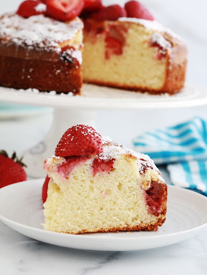 Gateau au yaourt et fraises fraiches coupe sur un plat a gateau et un morceau de gateau sur une assiette