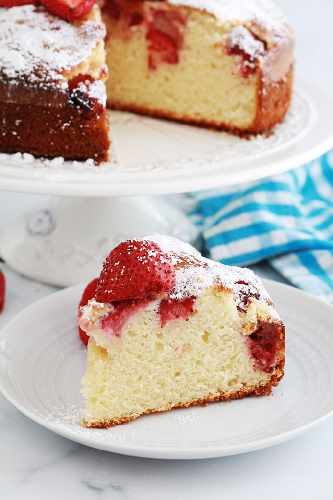 Gateau au yaourt et fraises fraiches coupe sur un plat a gateau et un morceau de gateau sur une assiette