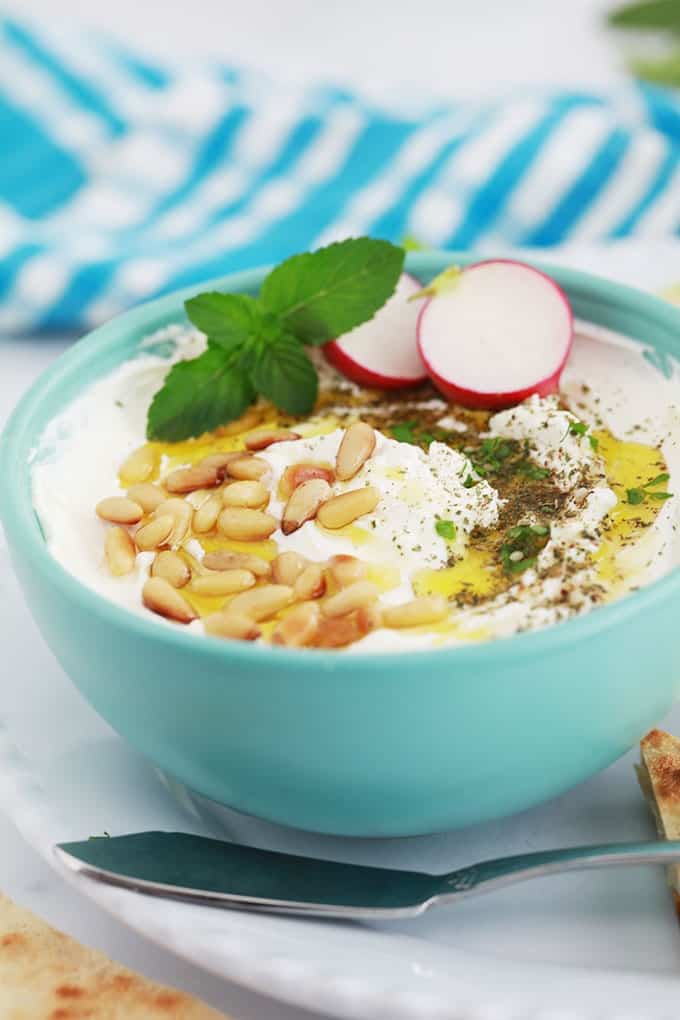 Labneh fait maison dans un bol, garni d'huile d'olive, oignons de pin grillés, zaatar, crudité