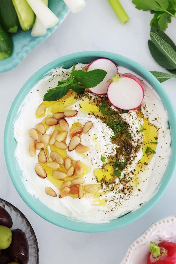 Labneh fait maison dans un bol, garni d'huile d'olive, oignons de pin grillés, zaatar et crudités