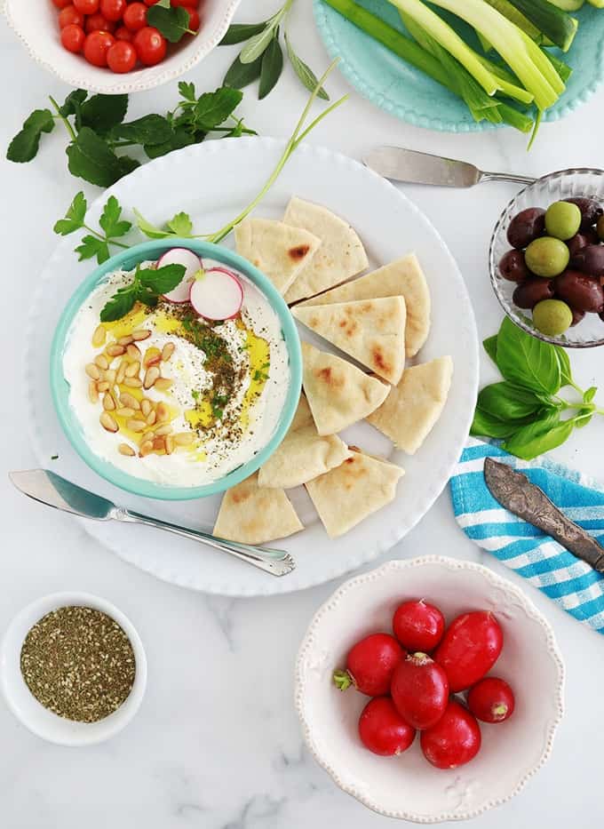 Labneh fait maison dans un bol, garni d'huile d'olive, oignons de pin grillés, zaatar, crudités et pain pita