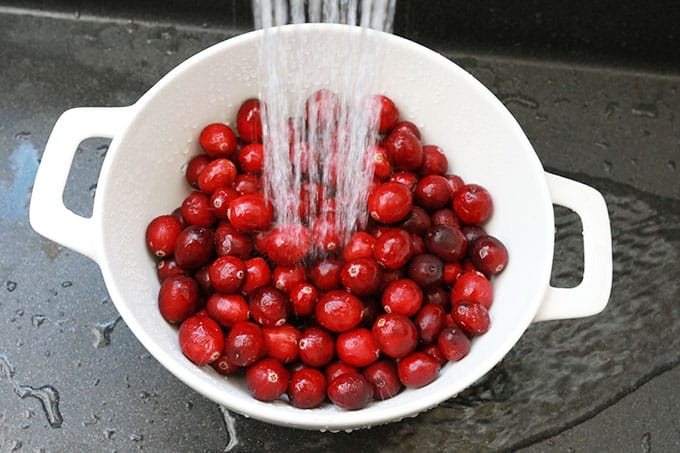 Canneberges fraîches (cranberries) dans une passoire lavées sous l;eau du robinet.