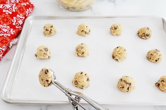 Boules de pâte à cookies américains déposées espacées dans une plaque en aluminium à l'aide d'une cuillère à biscuits