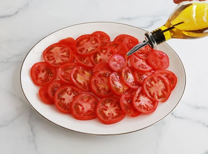Dans un plat de service, des rondelles de tomates assaisonnées d'huile d'olive