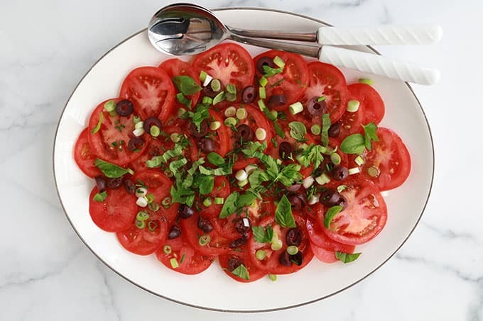 Dans un plat de service : salade de tomates fraîches avec olives, oignons, basilic, ciboulette, persil