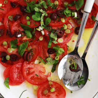 Dans un plat de service : salade de tomates fraîches avec olives, oignons, basilic, ciboulette, persil, huile d'olive et vinaigre