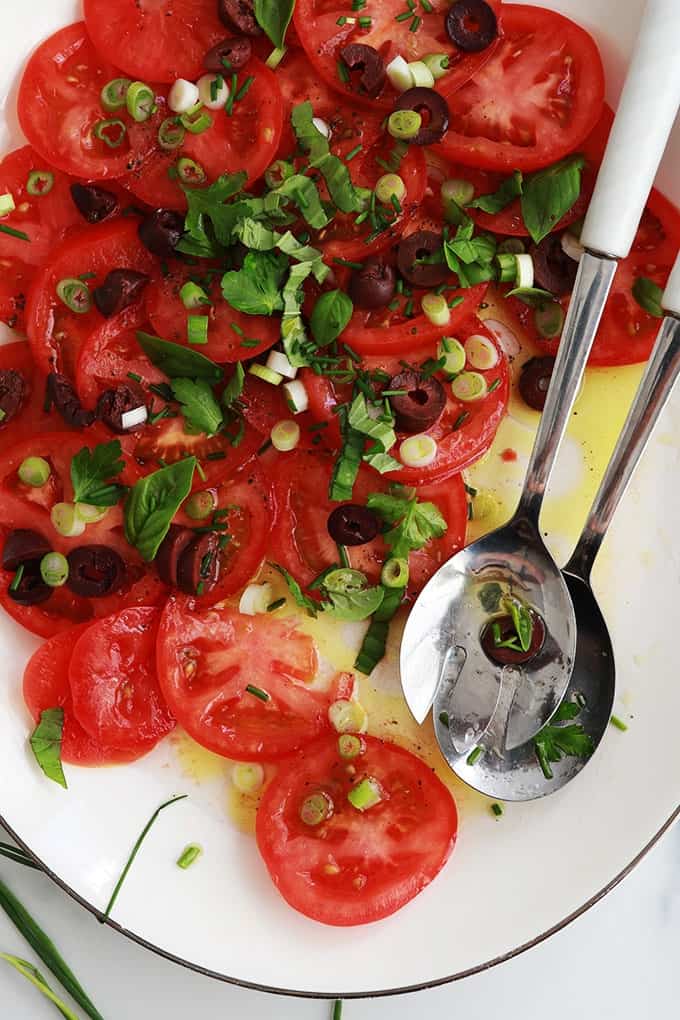 Dans un plat de service : salade de tomates fraîches avec olives, oignons, basilic, ciboulette, persil, huile d'olive et vinaigre
