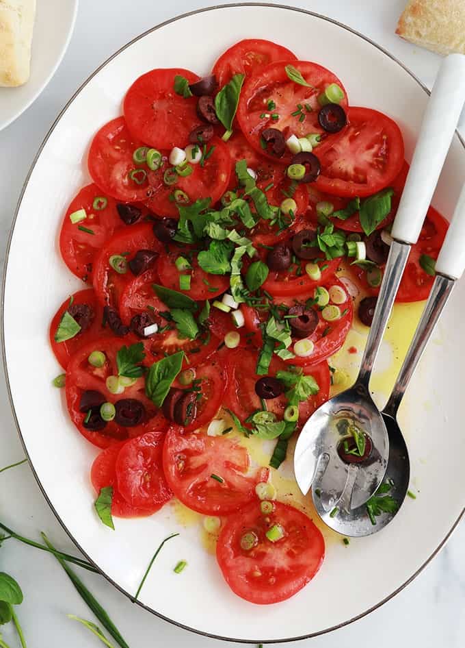 Dans un plat de service : salade de tomates fraîches avec olives, oignons, basilic, ciboulette, persil