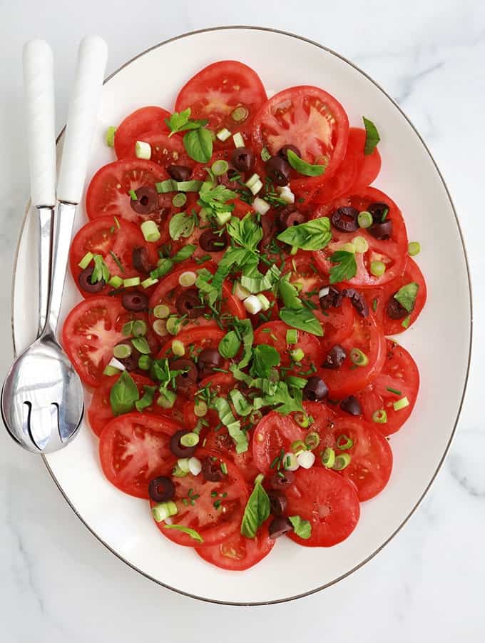 Dans un plat de service : salade de tomates fraîches avec olives, oignons, basilic, ciboulette, persil