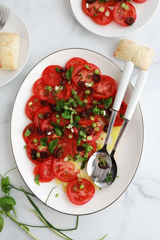Dans un plat de service : salade de tomates fraîches avec olives, oignons, basilic, ciboulette, persil