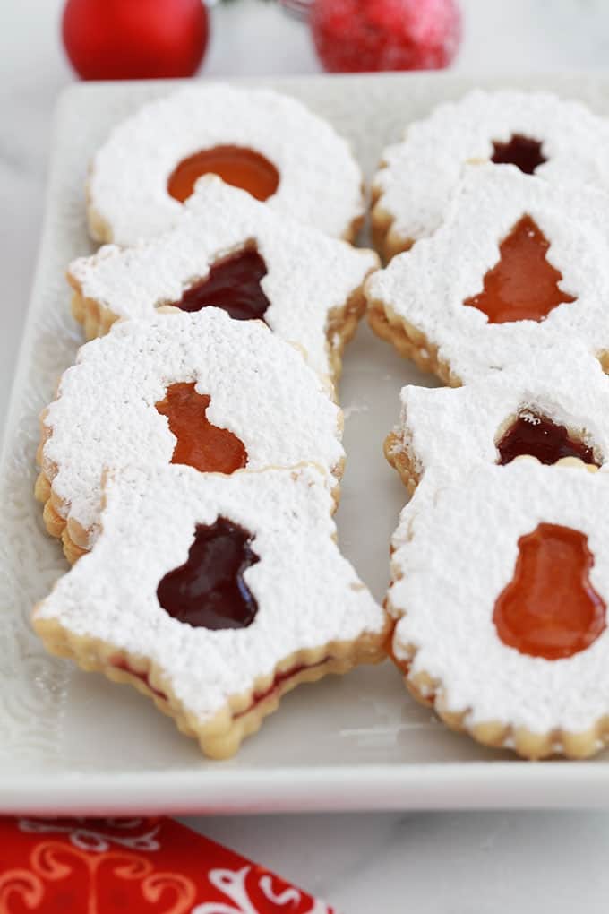 Sur un plat de service, des biscuits sablés de Noel Linzer à la confiture de framboise et confiture d'abricot.