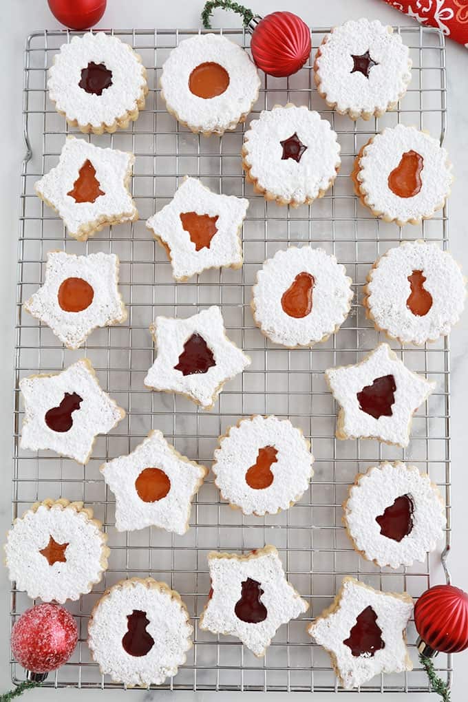 Sur une grille, des biscuits sablés de Noel Linzer à la confiture de framboise et confiture d'abricot.