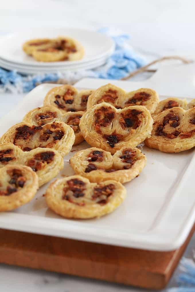 Dans un plat de service, des palmiers feuilletés pour apéro dînatoire, au pesto, tomates séchées, fromage feta et olives