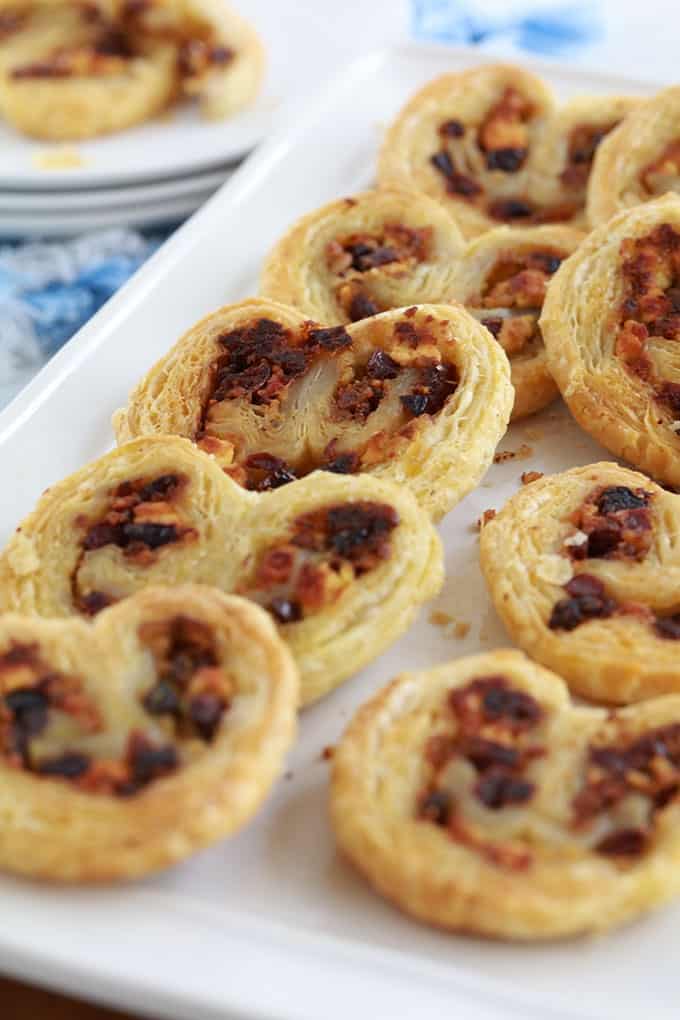 Dans un plat de service, des palmiers feuilletés pour apéro dînatoire, au pesto, tomates séchées, fromage feta et olives