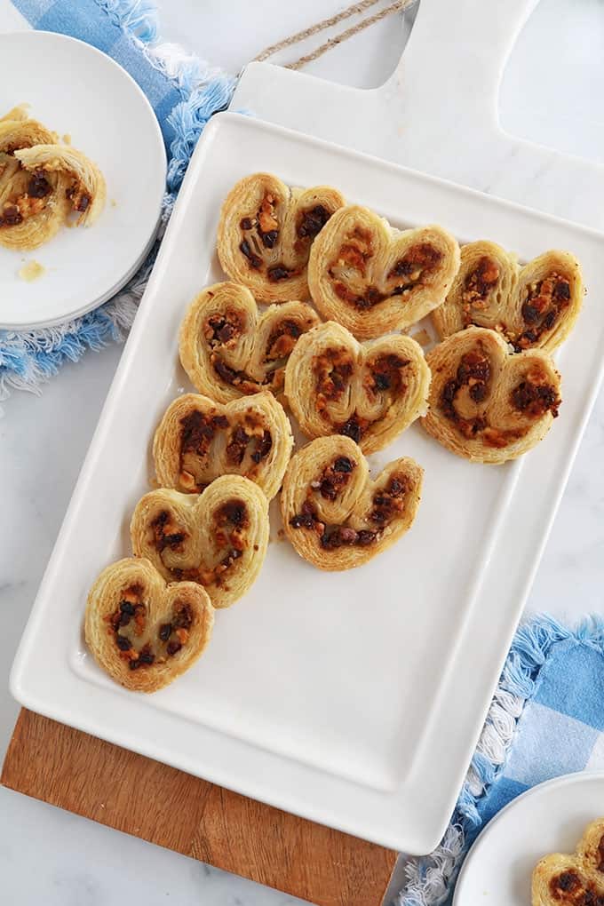 Dans un plat de service, des palmiers feuilletés pour apéro dînatoire, au pesto, tomates séchées, fromage feta et olives