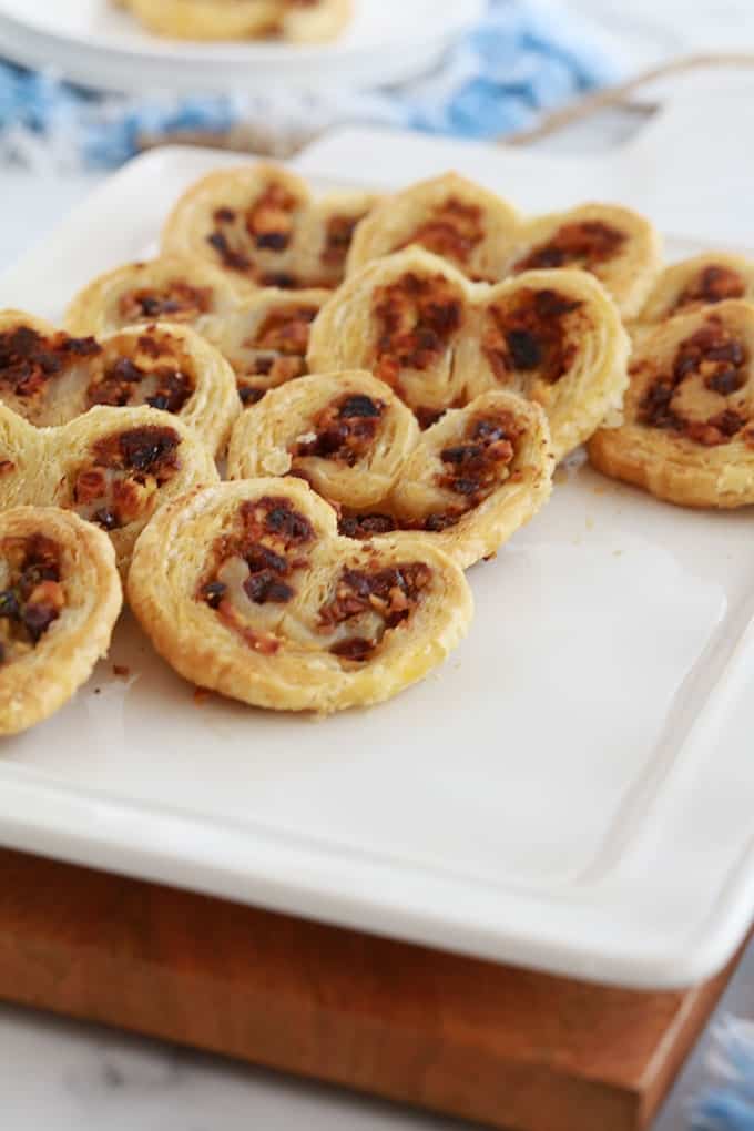 Dans un plat de service, des palmiers feuilletés pour apéro dînatoire, au pesto, tomates séchées, fromage feta et olives