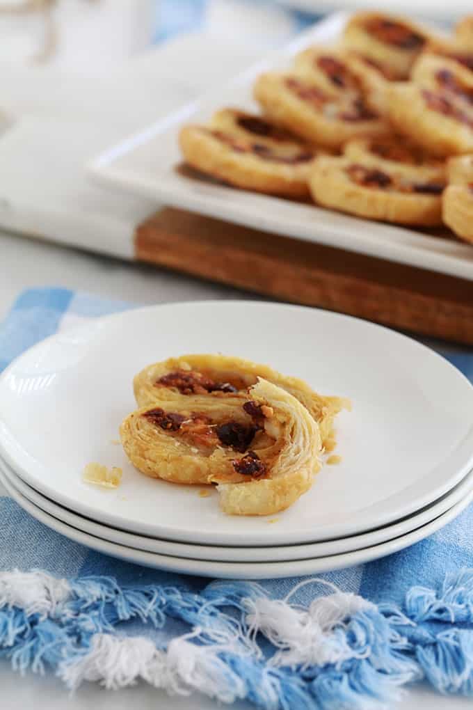 Dans une petite assiette, 2 palmiers feuilletés pour apéro dînatoire, au pesto, tomates séchées, fromage feta et olives