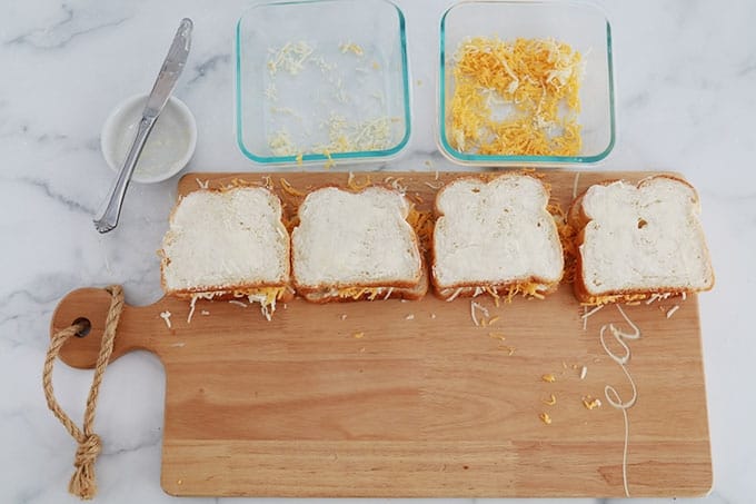 Sur un plan de travail, sandwichs assemblés constitués de deux tranches de pain beurrées et fourrées de fromages râpés.