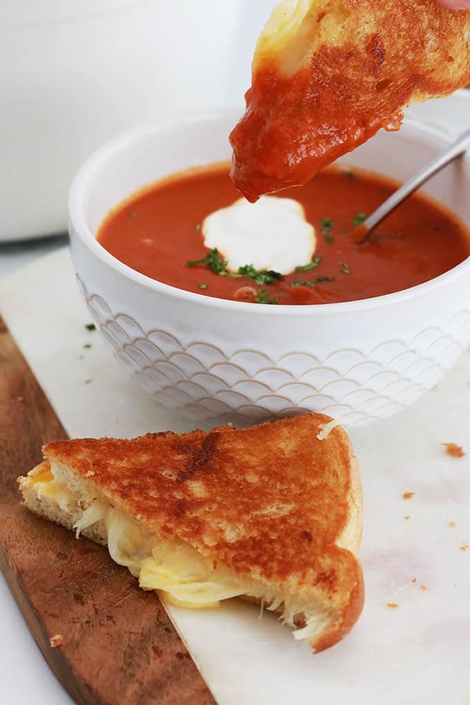 Sandwich au fromage fondu en morceaux, deux bols de soupe tomate.