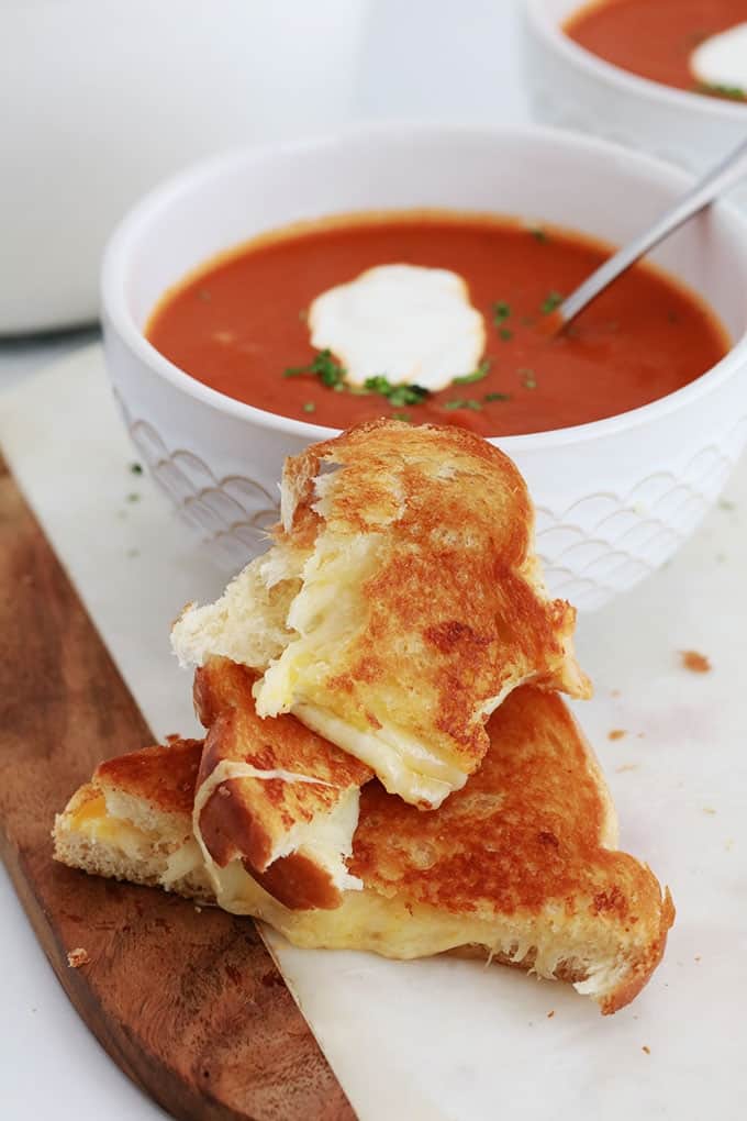 Sandwich Grilled Cheese coupé en morceaux et deux bols de soupe tomate.