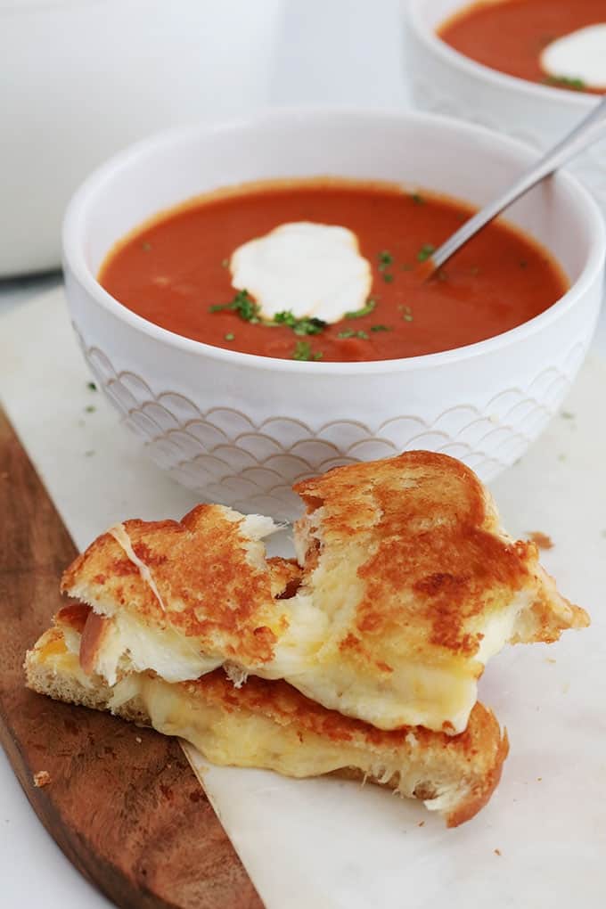 Sandwich grille au fromage fondu en morceaux et soupe de tomate dans deux bols.