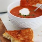 Soupe tomate maison dans des bols et dans une cocotte, avec un sandwich au fromage fondu (Grilled cheese sandwich).