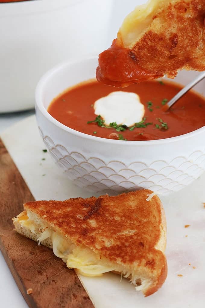 Soupe tomate maison dans des bols et dans une cocotte, avec un sandwich au fromage fondu (Grilled cheese sandwich).