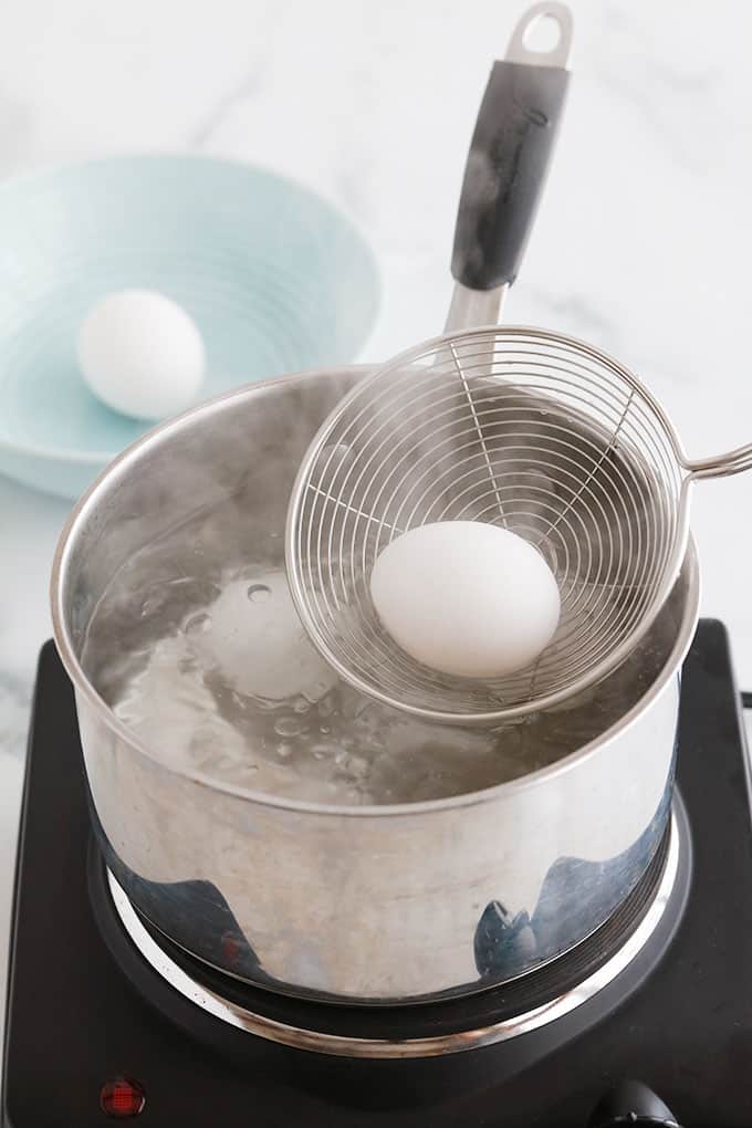 2 oeufs dans une casserole d'eau bouillante, 1 oeuf dans un bol bleu, un oeuf dans une spatule.