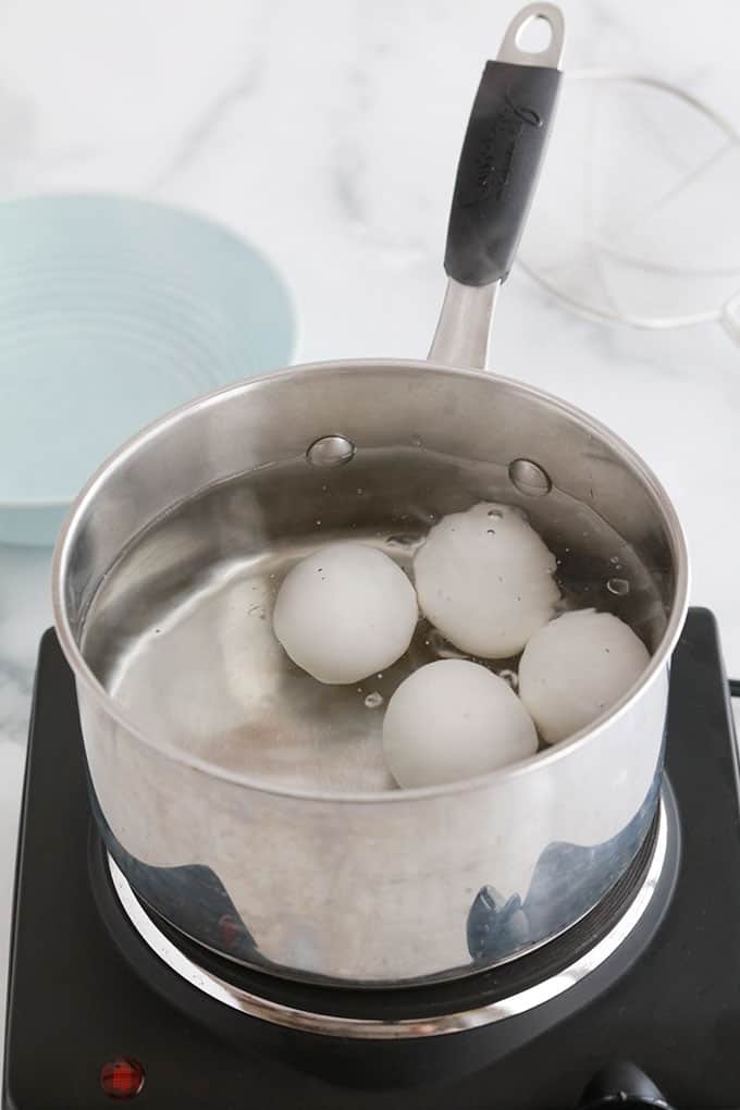 4 gros oeufs en train de cuire dans une casserole d'eau à frémissement.