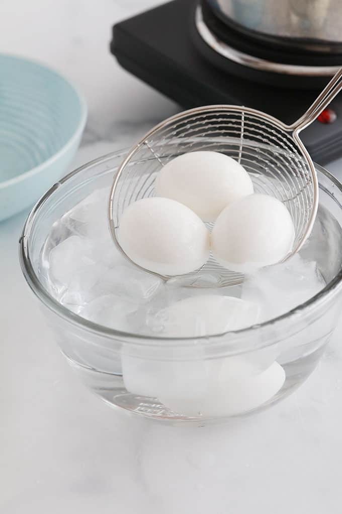 Un bol d'eau glacée et un oeuf dur. 3 oeufs durs dans une spatule à plonger dans l'eau glacée.