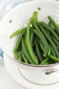Haricots verts blanchis dans une passoire blanche.